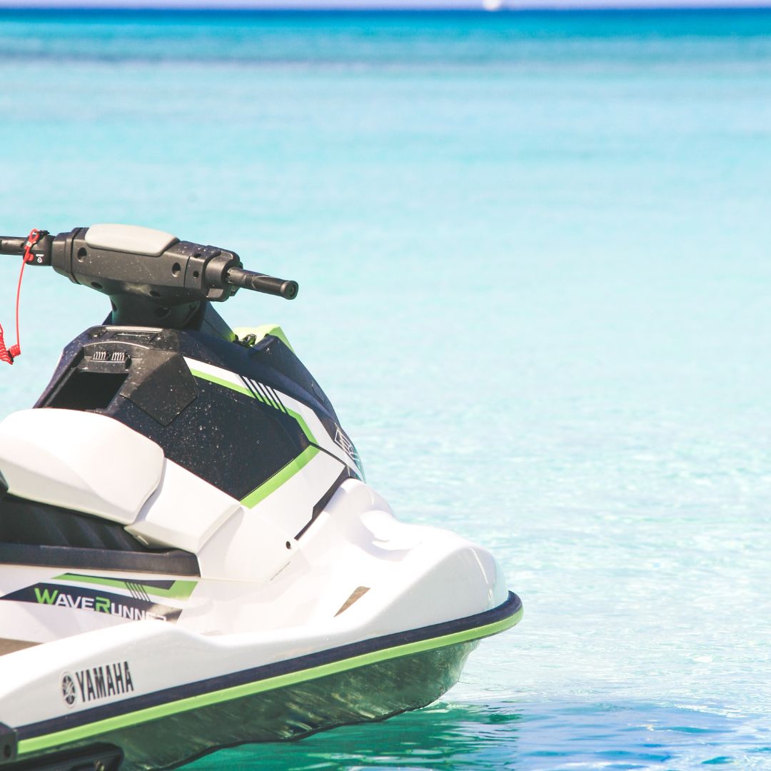 A white and green Yamaha jet ski is floating on crystal-clear turquoise water. The jet ski is stationary, and no rider is visible in the image, giving the impression of peacefulness and the potential for leisure activities in a serene aquatic environment.