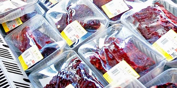 Close-up of several packages of dolphin meat on display, each labeled with a price tag, in a supermarket setting.