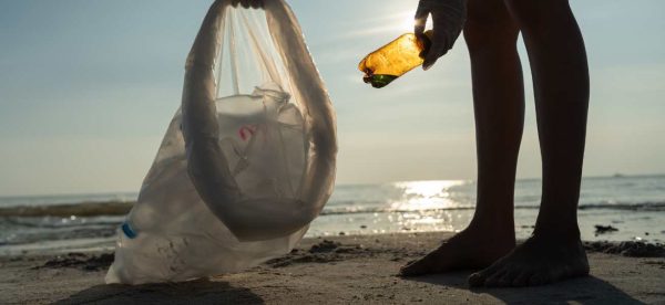 Photo of a person picking up plastic pollution on a beach. Only legs of the person are shown