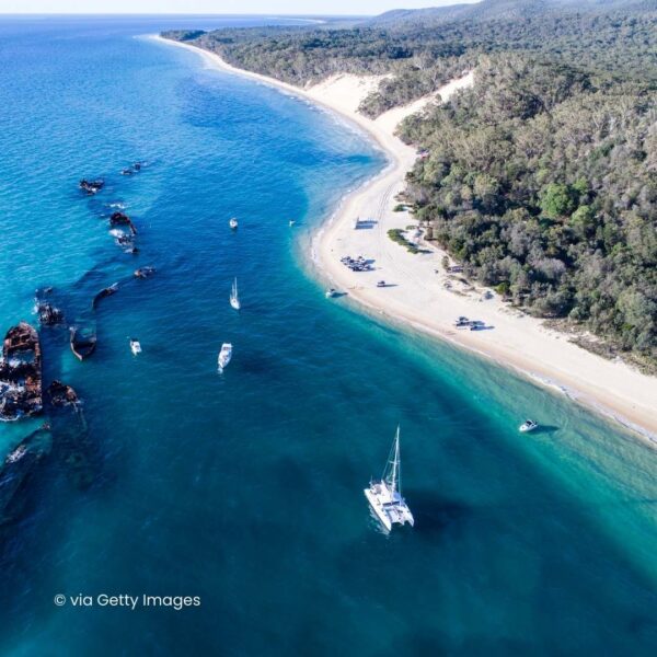 Aerial shot of blue green ocean meeting sand and trees. Boats on the ocean