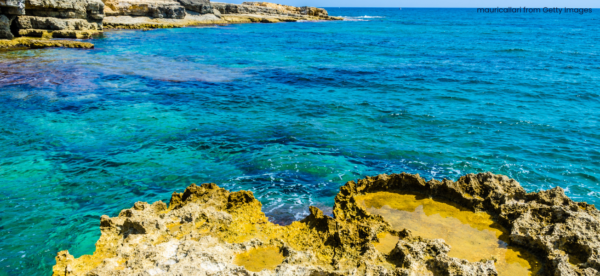 Sunlight appearing on the rocky shores in a bay with water and coral being visible 