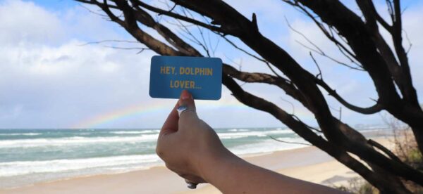 Hand holding card saying "hey dolphin lover" at the beach