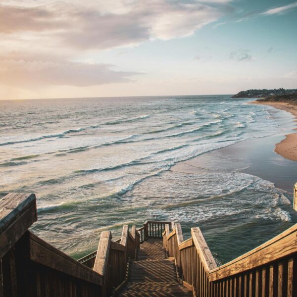 Wooden steps and rails lead down to a beach. The sun is setting