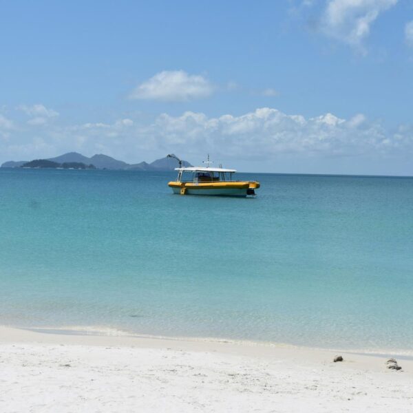 Single boat on top of calm green water, Sand is in the forefront and a island is seen in the distance